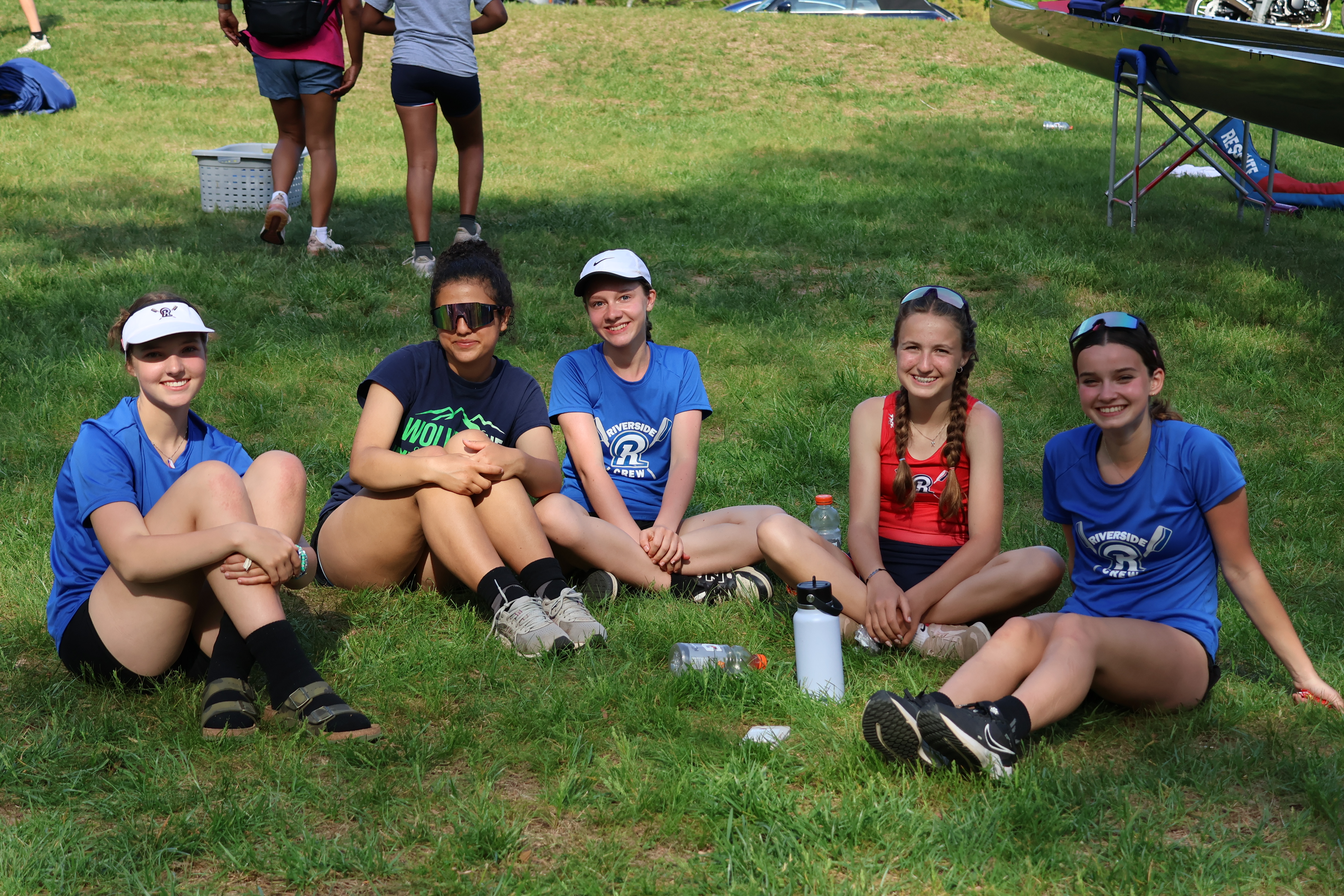 Five Riverside teammates smiling and relaxing together on the grass at a regatta